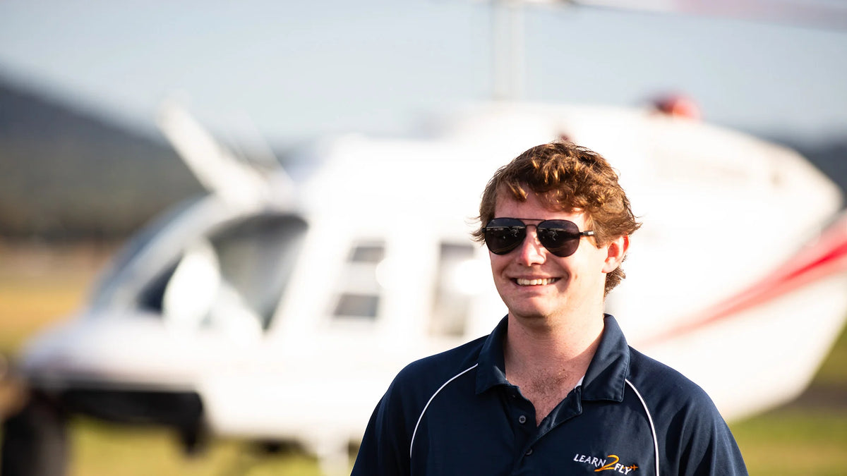 Man in sunglasses and a dark shirt standing in front of a helicopter