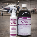 Two bottles of ACF-50 Anti-Corrosion Formula, one in a white spray bottle and one in a large dark bottle, displayed in front of a blurred airplane hangar background.