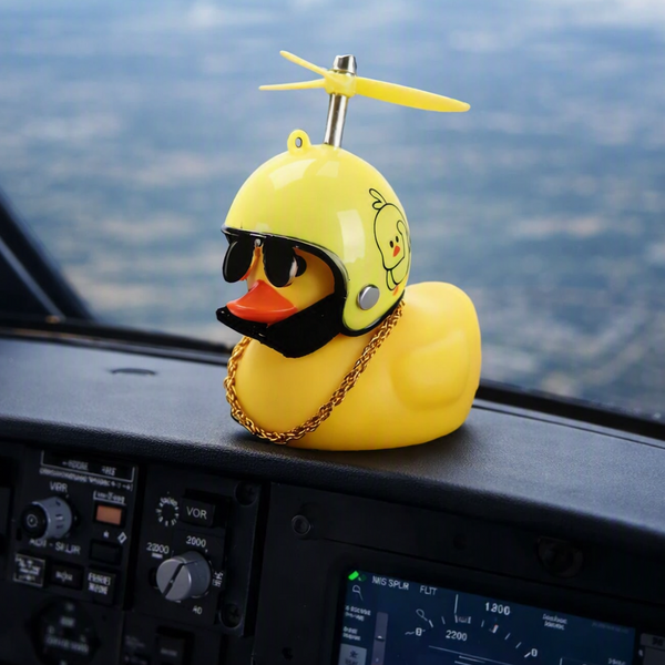 A yellow rubber duck styled like a duck wearing a yellow helmet, black sunglasses, and a gold chain, placed on a airplane dashboard with the window showing the sky and landscape outside. A 'Made with AI' badge is in the top right corner.