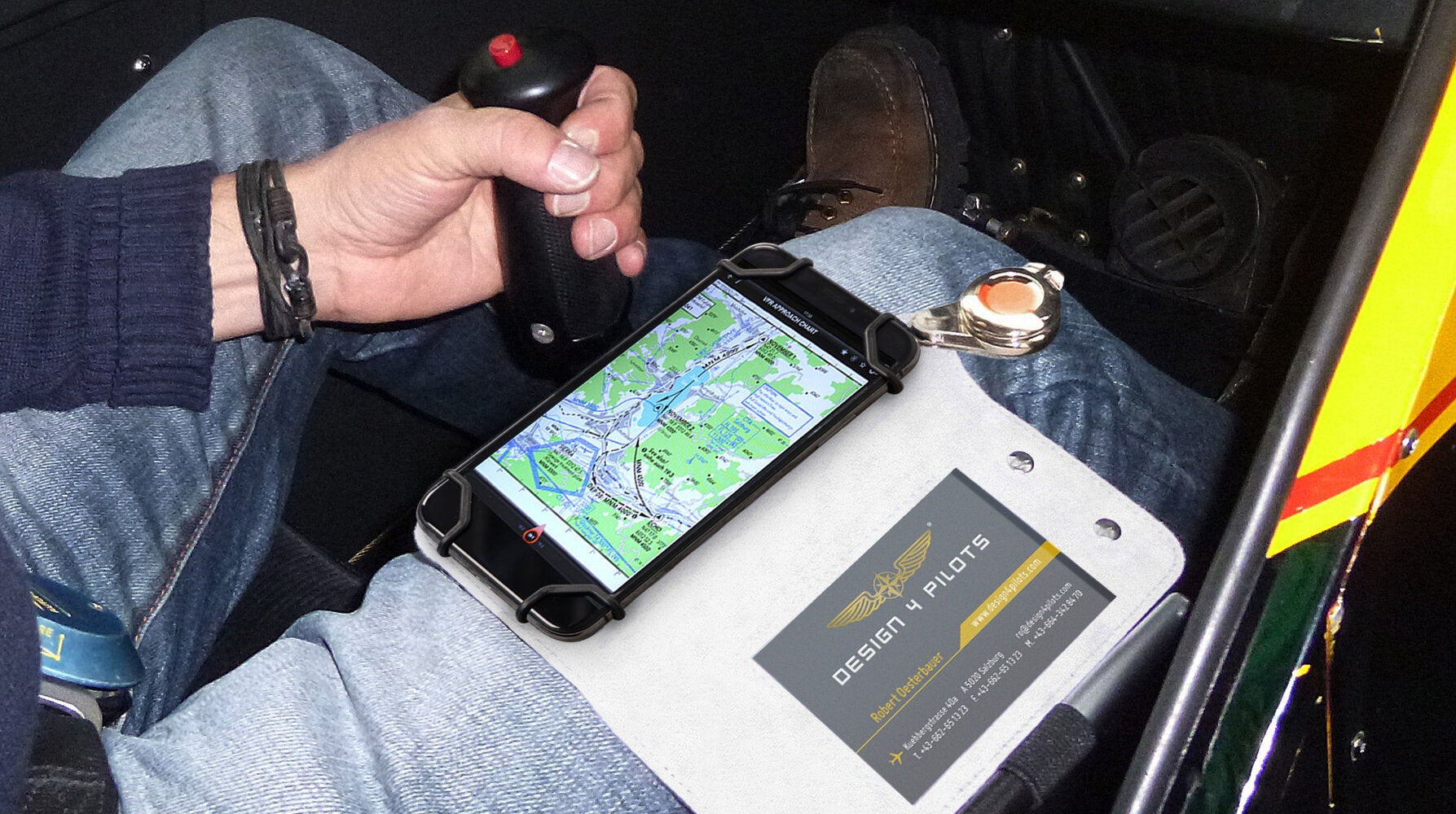Person inside a helicopter cockpit with a smartphone displaying a map and a business card on a tablet.